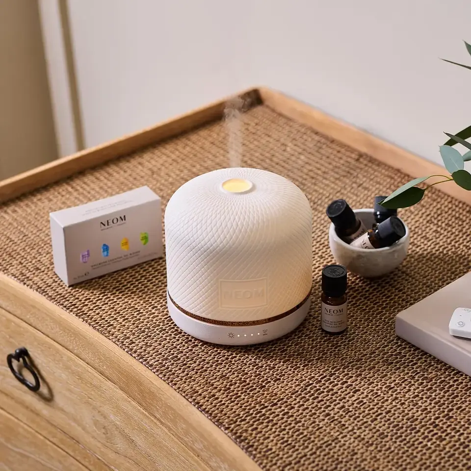 White diffuser on a woven mat with essential oils and a NEOM box nearby.