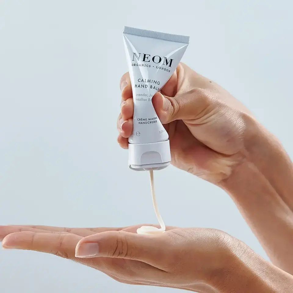 Hands squeezing Neom Calming Hand Balm onto palm.