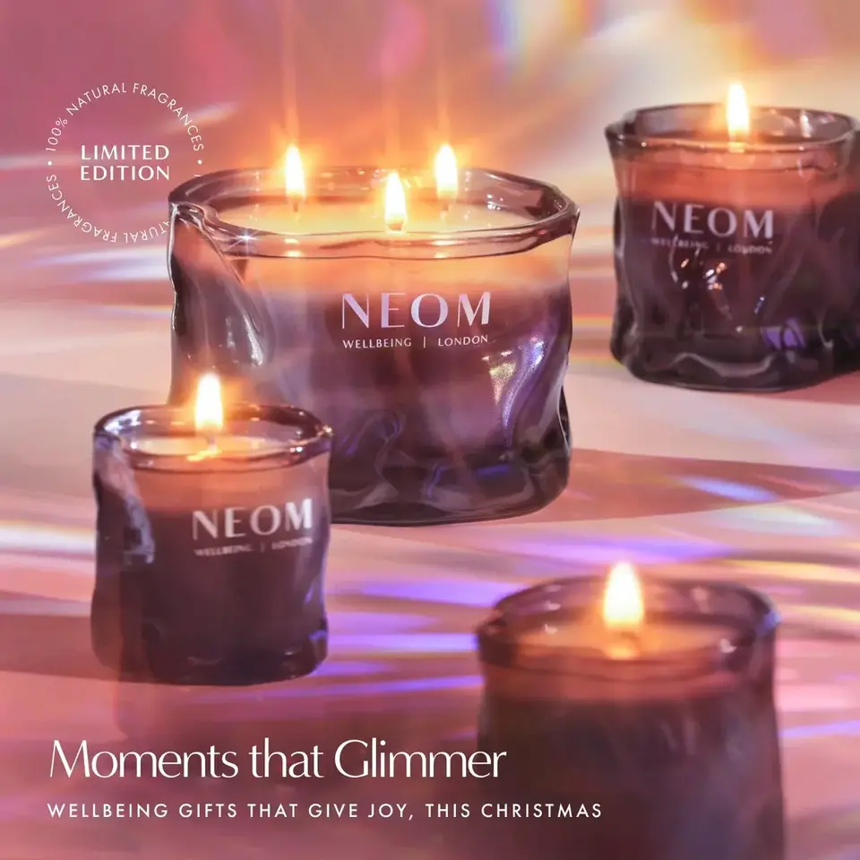Lit NEOM candles in glass holders with text: "Moments that Glimmer".