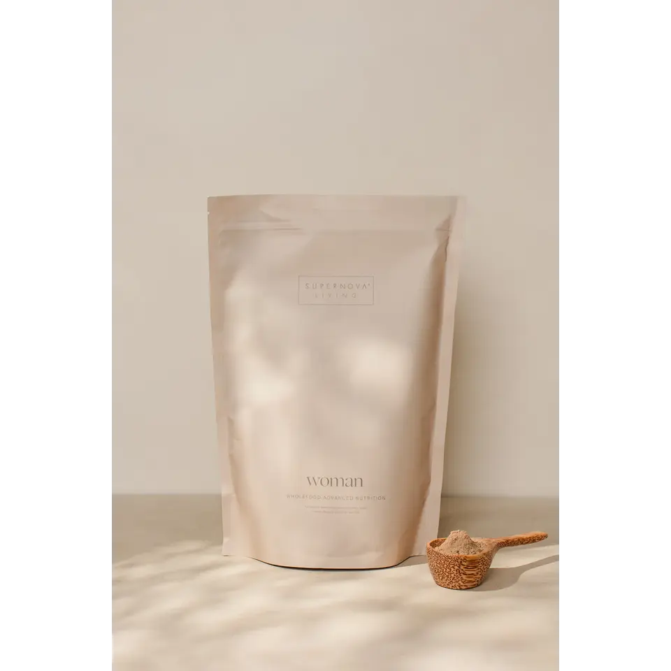 Supernova Living Woman supplement pouch with a wooden scoop of powder on a light surface.