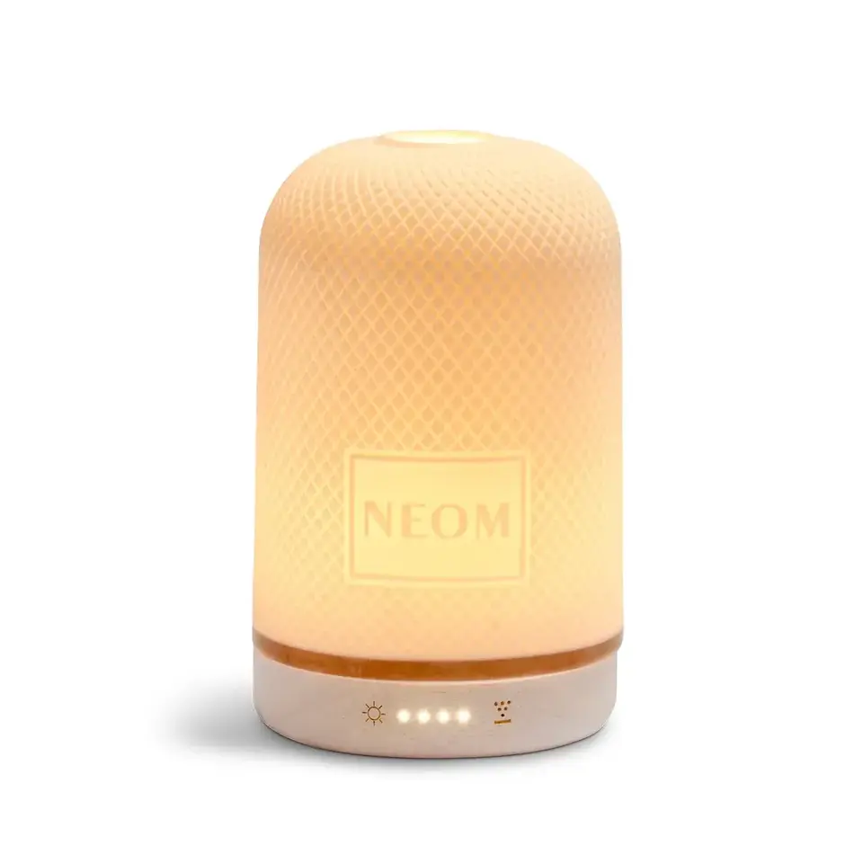 Illuminated NEOM diffuser with textured surface and control icons at the base.