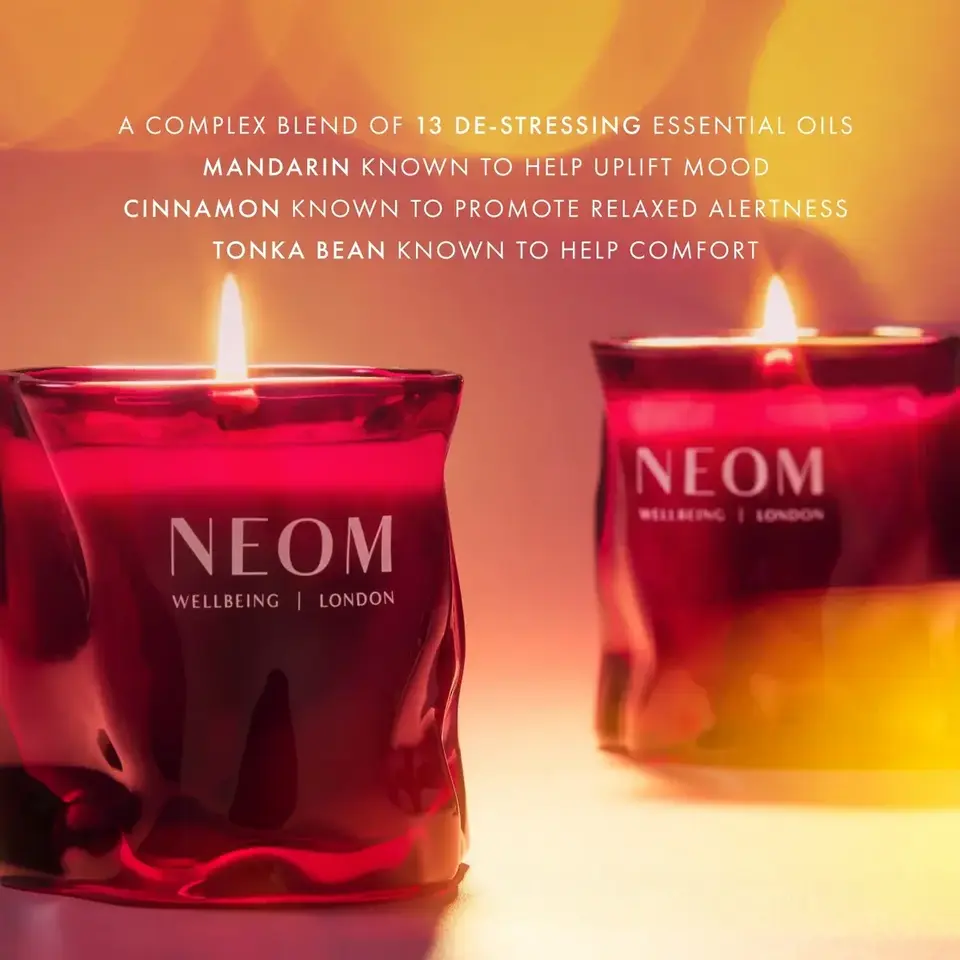 Red NEOM candles with flames, text about essential oils: mandarin, cinnamon, tonka bean.