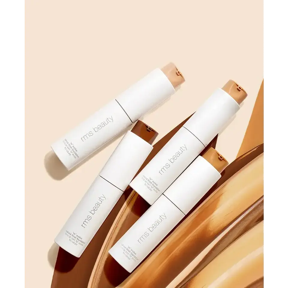 Four rms beauty foundation bottles on a beige background with swatches.