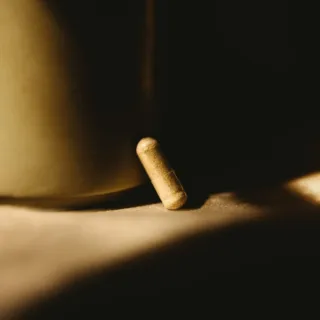A single capsule rests on a surface, partially lit by warm light.