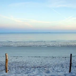 Sandy beach with calm sea and clear sky, two wooden posts in foreground.