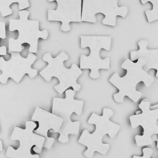 Scattered white jigsaw puzzle pieces on a plain surface.