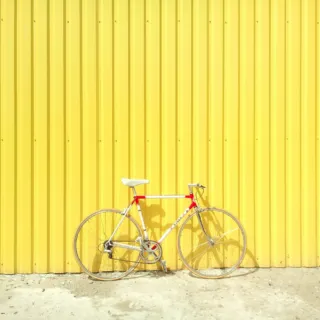 Bicycle with red and white frame against a yellow corrugated metal wall.