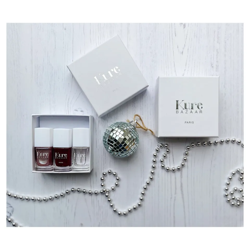 Kure Bazaar nail polish set with disco ball and silver beads on white wood background.