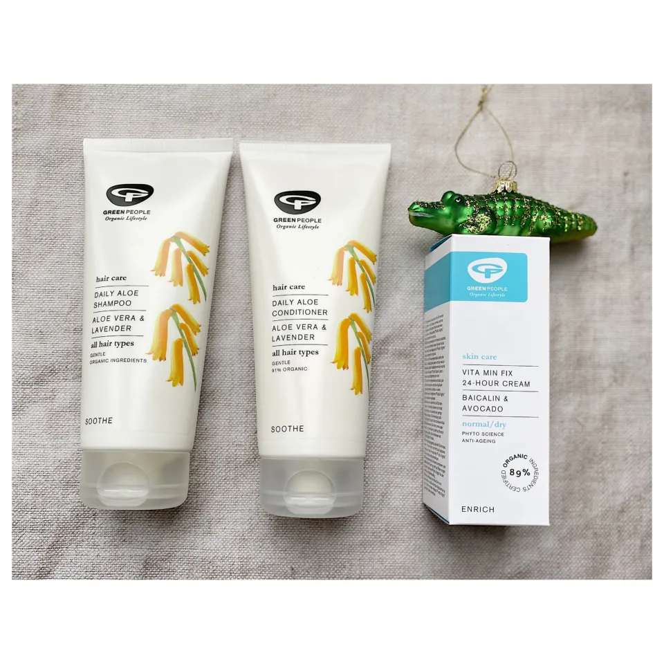 Green People shampoo, conditioner, and cream on a grey fabric background with a green crocodile ornament.