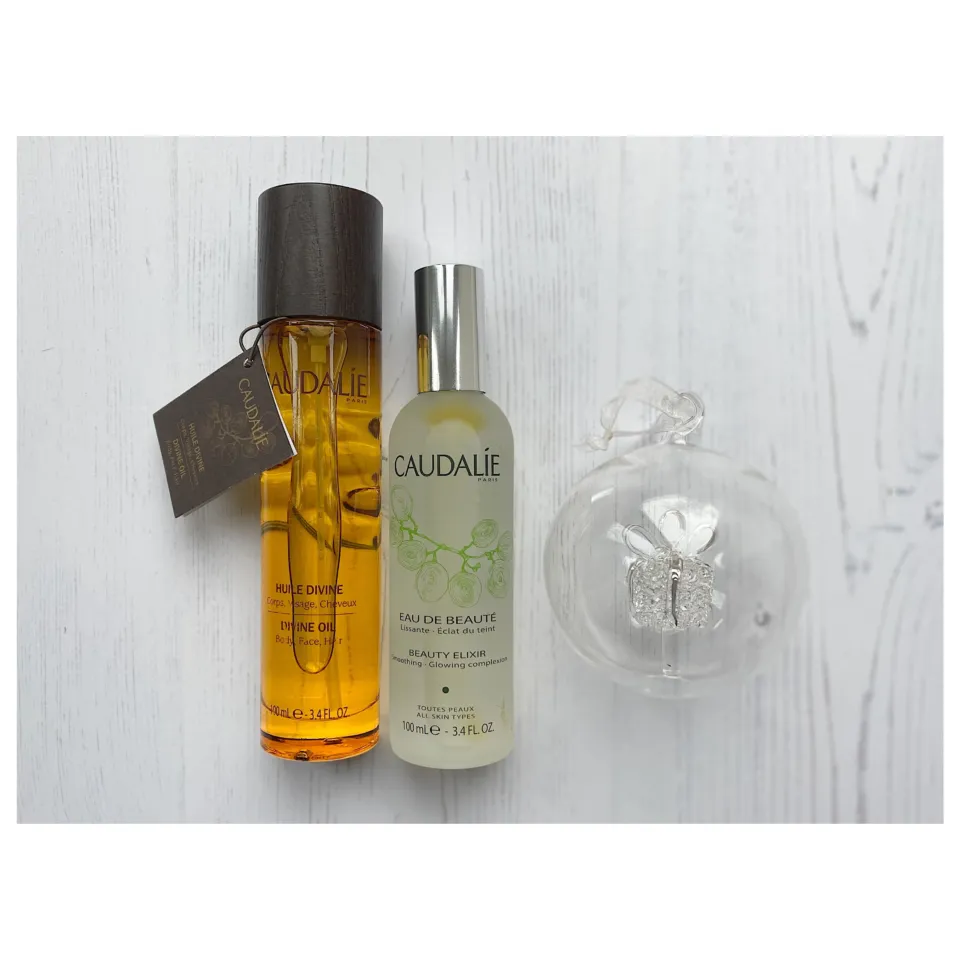 Caudalie Divine Oil and Beauty Elixir bottles on white wood surface.