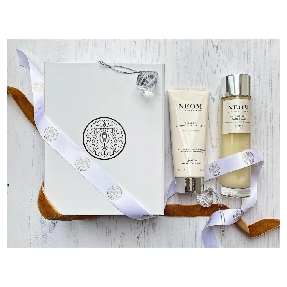 Neom gift set with body butter and bath foam on white wood background.