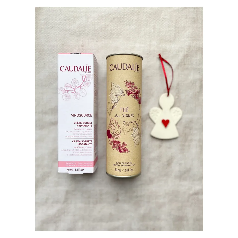 Caudalie Vinosource cream and Thé des Vignes fragrance with angel ornament on fabric background.