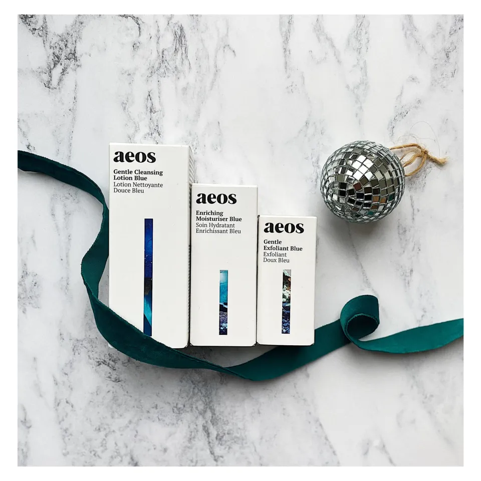 Three aeos skincare boxes on marble with a teal ribbon and disco ball.