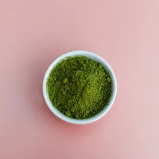 Green powder in a white bowl on a pink background.