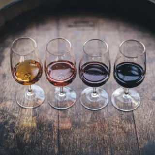 Four wine glasses with different coloured wines on a wooden barrel.