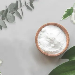 Wooden bowl of white powder surrounded by green leaves and white capsules.