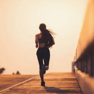 Person running on a bridge at sunset, wearing athletic clothing.