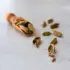 Cardamom pods scattered on a light grey surface with a wooden scoop.