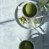 Two cups of green tea on a table, one with matcha powder and a spoon on a saucer.