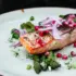 Grilled salmon with asparagus, red onion, pomegranate seeds, and herbs on a light green plate.
