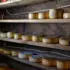 Rounds of cheese ageing on wooden shelves in a rustic cellar.