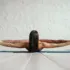 Person practising yoga, lying on a mat, holding feet with legs extended wide.