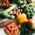 Assorted fresh vegetables including peppers, broccoli, avocado, and sweet potatoes on a white surface.