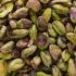 Close-up of unshelled pistachio nuts with green and purple hues.
