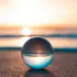 Glass sphere on sand reflecting sunset over the sea.