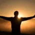 Silhouette of person with arms outstretched at sunrise over misty landscape.