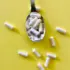 White capsules on a spoon and scattered on a yellow background.