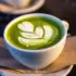Green matcha latte with white leaf latte art in a white cup on a napkin.