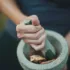 Hand using a mortar and pestle to grind dried leaves.