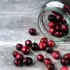 Glass jar tipped over with cranberries spilling onto a wooden surface.