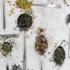 Spoons with various loose leaf teas and herbs on a marble surface.