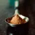Spoonful of brown powder on a dark surface.