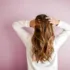 Person with long wavy hair facing a pink wall, wearing a white top.