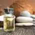 Glass bottle of oil on wooden surface, with coconuts and white stones in background.