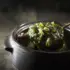Steaming green vegetable soup in a black ceramic bowl with a wooden spoon.