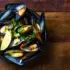Bowl of mussels with lemon wedge and herbs on wooden table.