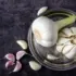 Whole and peeled garlic on a silver tray with scattered cloves on a dark surface.