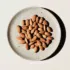 Almonds on a speckled ceramic plate against a light background.