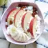 Bowl with apple slices, banana, raisins, and cottage cheese on a checkered cloth.