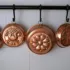 Copper moulds with embossed designs hanging on a black rail against white tiles.