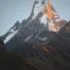 Snow-capped mountain peak at sunrise with orange light on the summit.