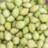 Green cardamom pods in a glass bowl on a textured surface.