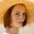 Woman with freckles wearing a large straw hat outdoors.
