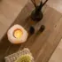 Wooden table with a lit candle, essential oils, reed diffuser, and a dry brush on a woven mat.