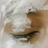 Closed eye with white clay mask applied on skin.