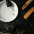 Dropper on white dish, wooden blocks, rosemary, and bottle on black marble surface.